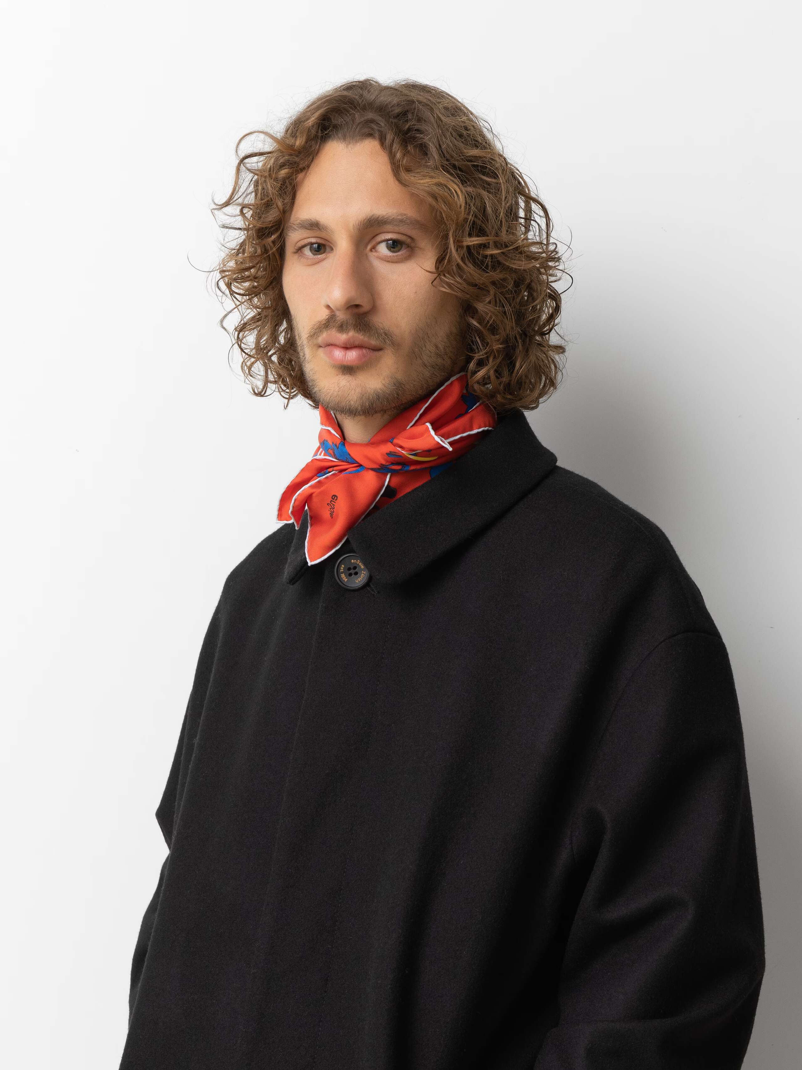 Picture of a male model wearing a black coat in combination with a orange red silk foulard
