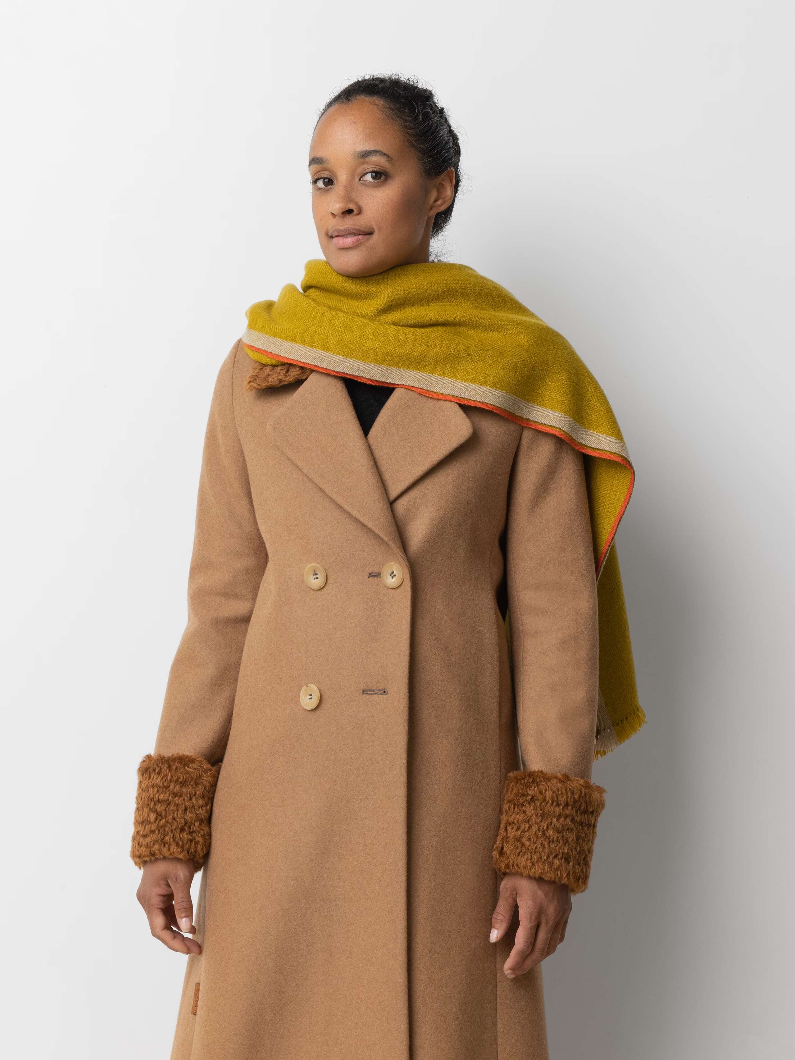 Picture of a female model wearing a beige wool coat in combination with a yellow cashmere scarf