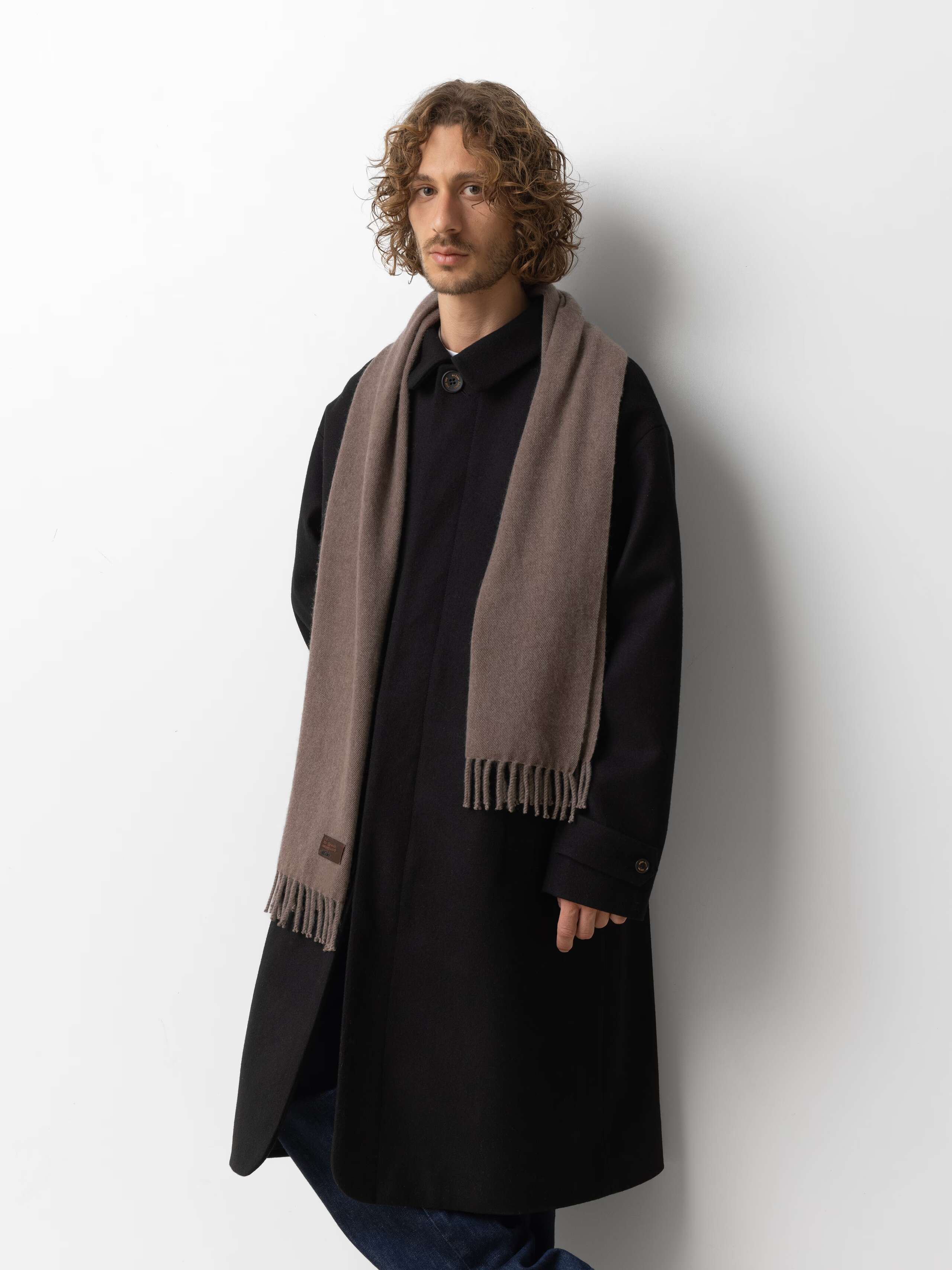 Picture of a male model wearing a black wool coat in combination with a beige cashmere scarf