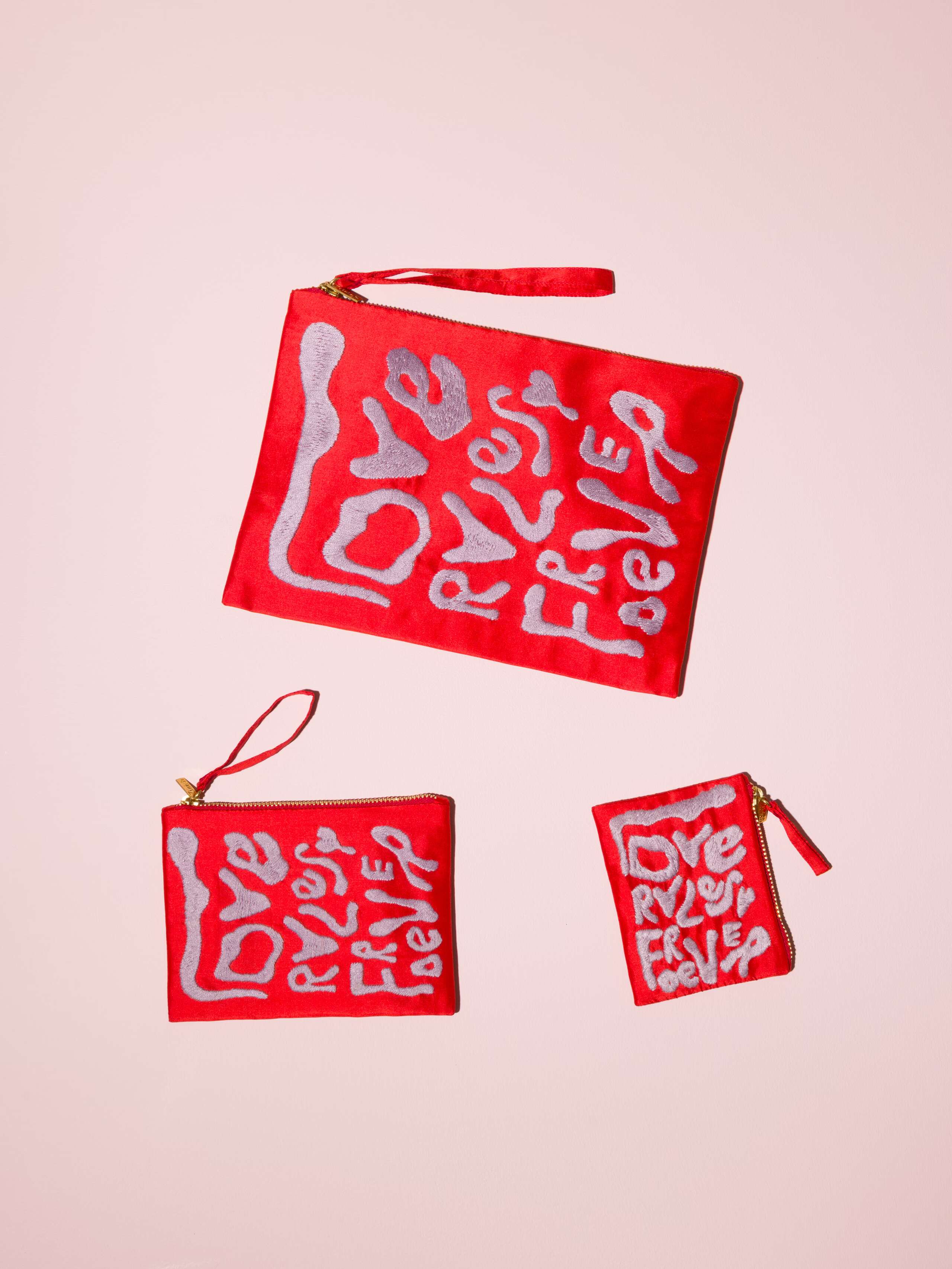 Picture of three red silk clutches featuring the motto Love Rules Forever