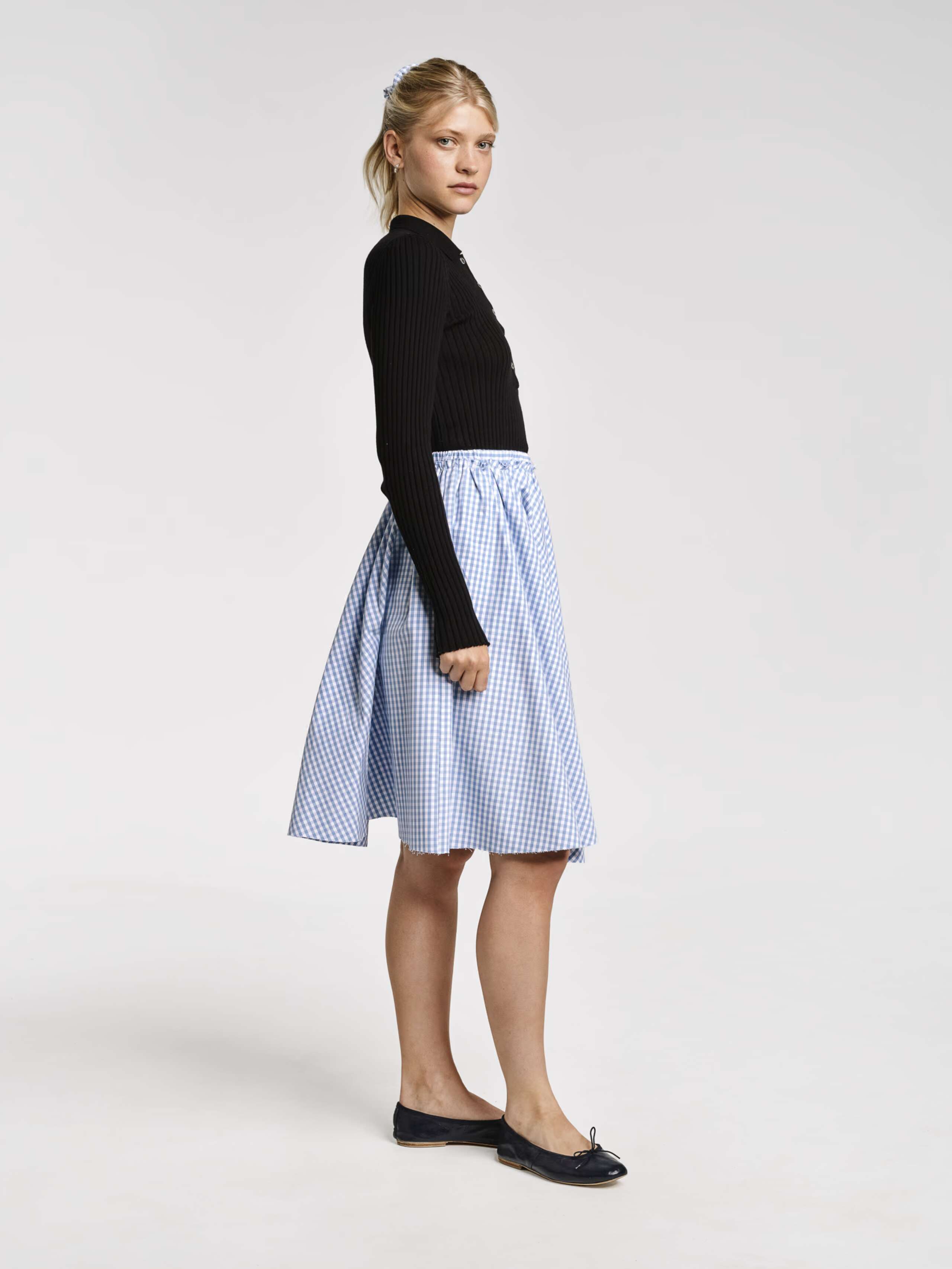 Model wearing the berta medium skirt in cerulean light blue vichy check cotton and venetia polo neck