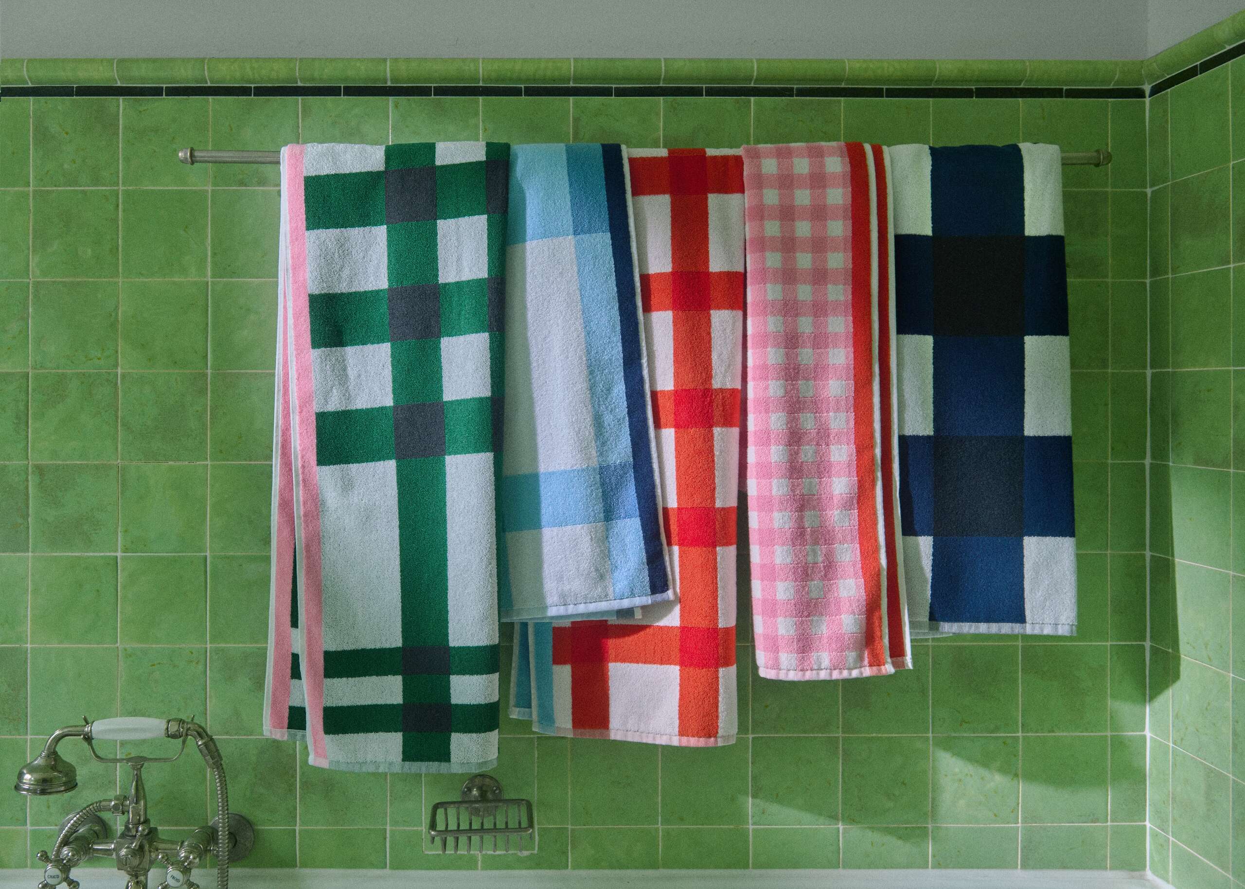 Picture of five colourful bath towels in a green tiled bathroom 